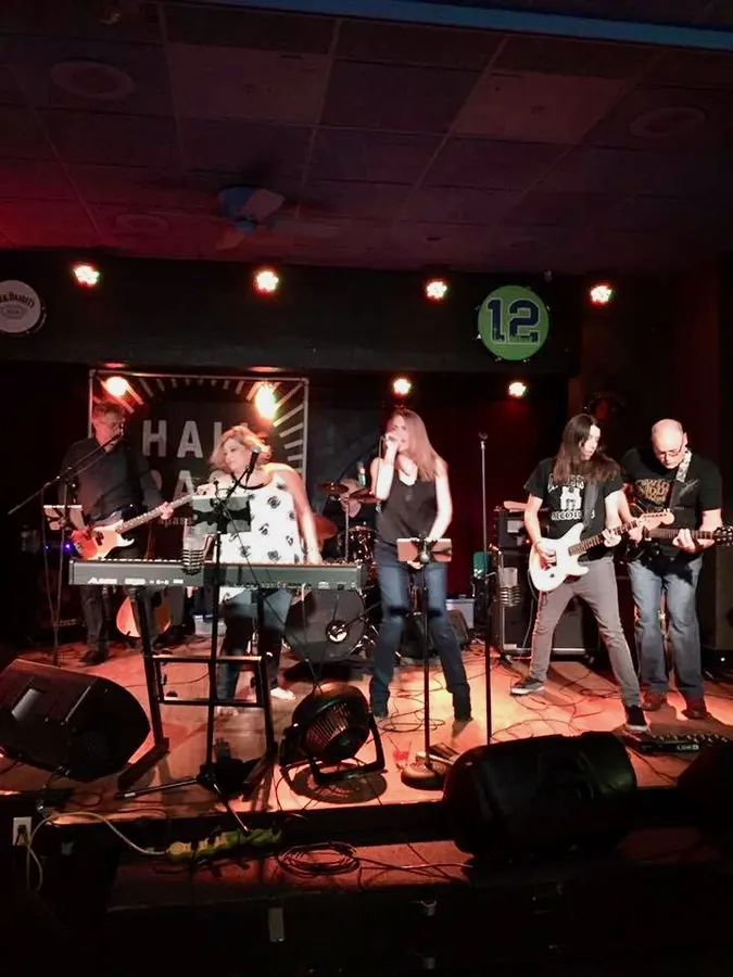A five-piece band on a club stage with keyboards and guitars