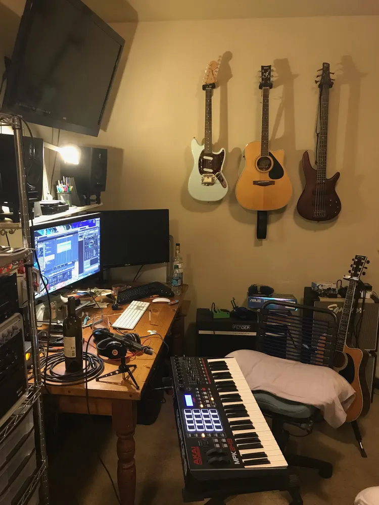 A home studio: guitars on the wall, monitors, an audio interface and a keyboard