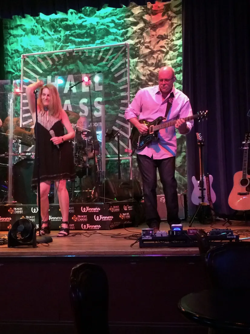 A singer and a guitarist performing on a club stage under green and purple light